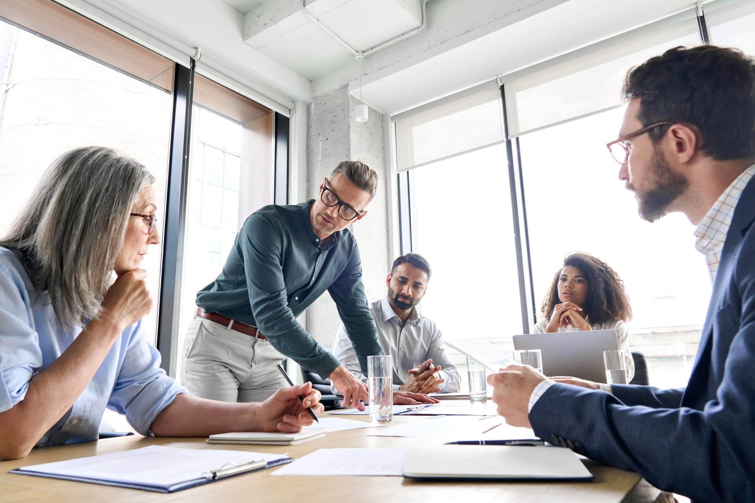 Male,Mature,Caucasian,Ceo,Businessman,Leader,With,Diverse,Coworkers,Team, Group of people discussing at a table