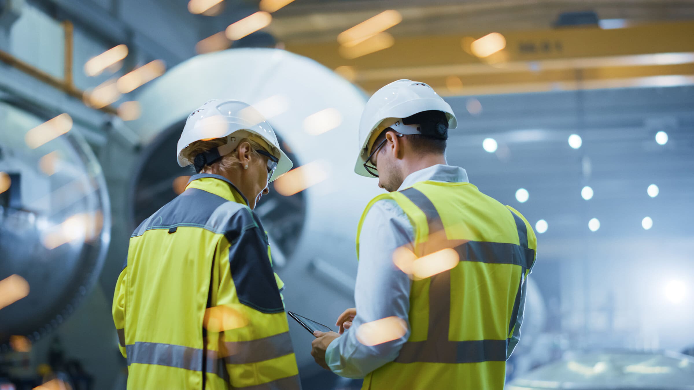 Two,Heavy,Industry,Engineers,Stand,In,Pipe,Manufacturing,Factory,,Use Two Heavy Industry Engineers Stand in Pipe Manufacturing Factory, Use Digital Tablet Computer, Have Discussion. Construction of Oil, Gas and Fuels Transport Pipeline. Back View Sparks Flying