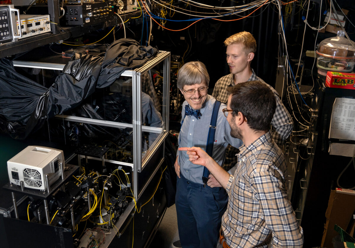 Paul Kwiat, left, works with his graduate students, Colin Lualdi, far right, and Nathan Arnold in the Kwiat Quantum Information Lab on July 25, 2024. The three were standing next to an ultra-long, free-space cavity. Frequency-entangled photons in the cavity bounce back and forth hundreds of times to achieve 1.2 kilometers of path length in a compact space.