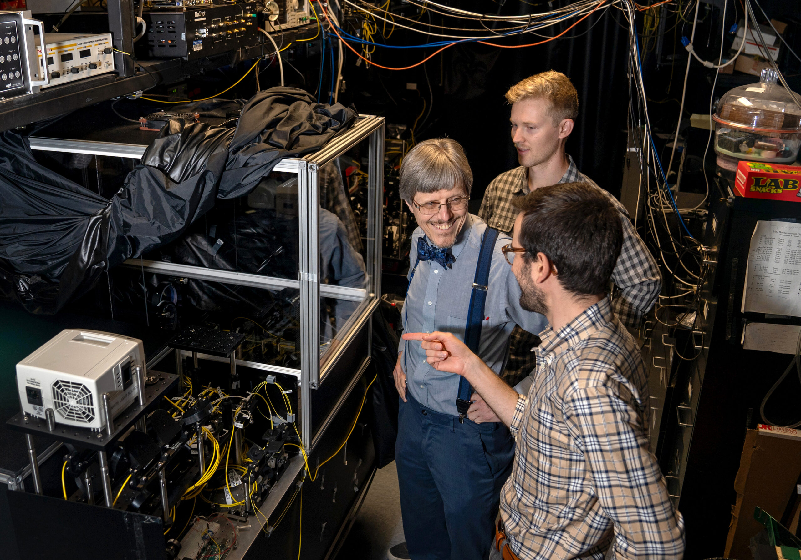Paul Kwiat, left, works with his graduate students, Colin Lualdi, far right, and Nathan Arnold in the Kwiat Quantum Information Lab on July 25, 2024. The three were standing next to an ultra-long, free-space cavity. Frequency-entangled photons in the cavity bounce back and forth hundreds of times to achieve 1.2 kilometers of path length in a compact space.